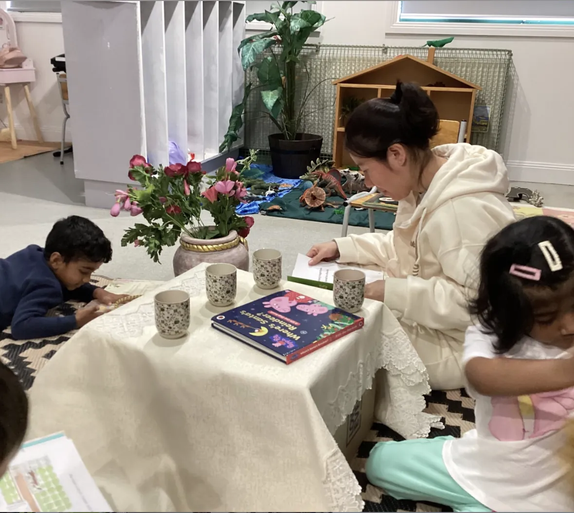 Educator reading picture books with children beside fresh flowers at Little Sharkies