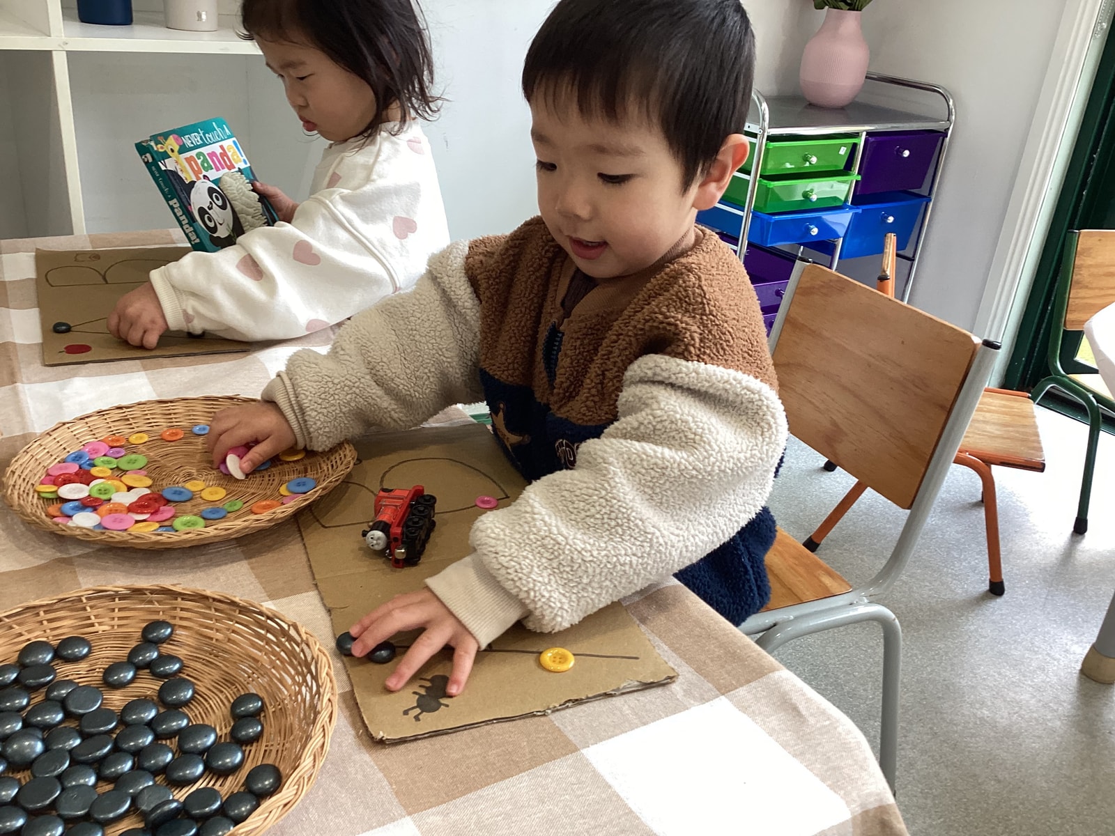 Toddler exploring buttons, stones and a train on a cardboard learning board